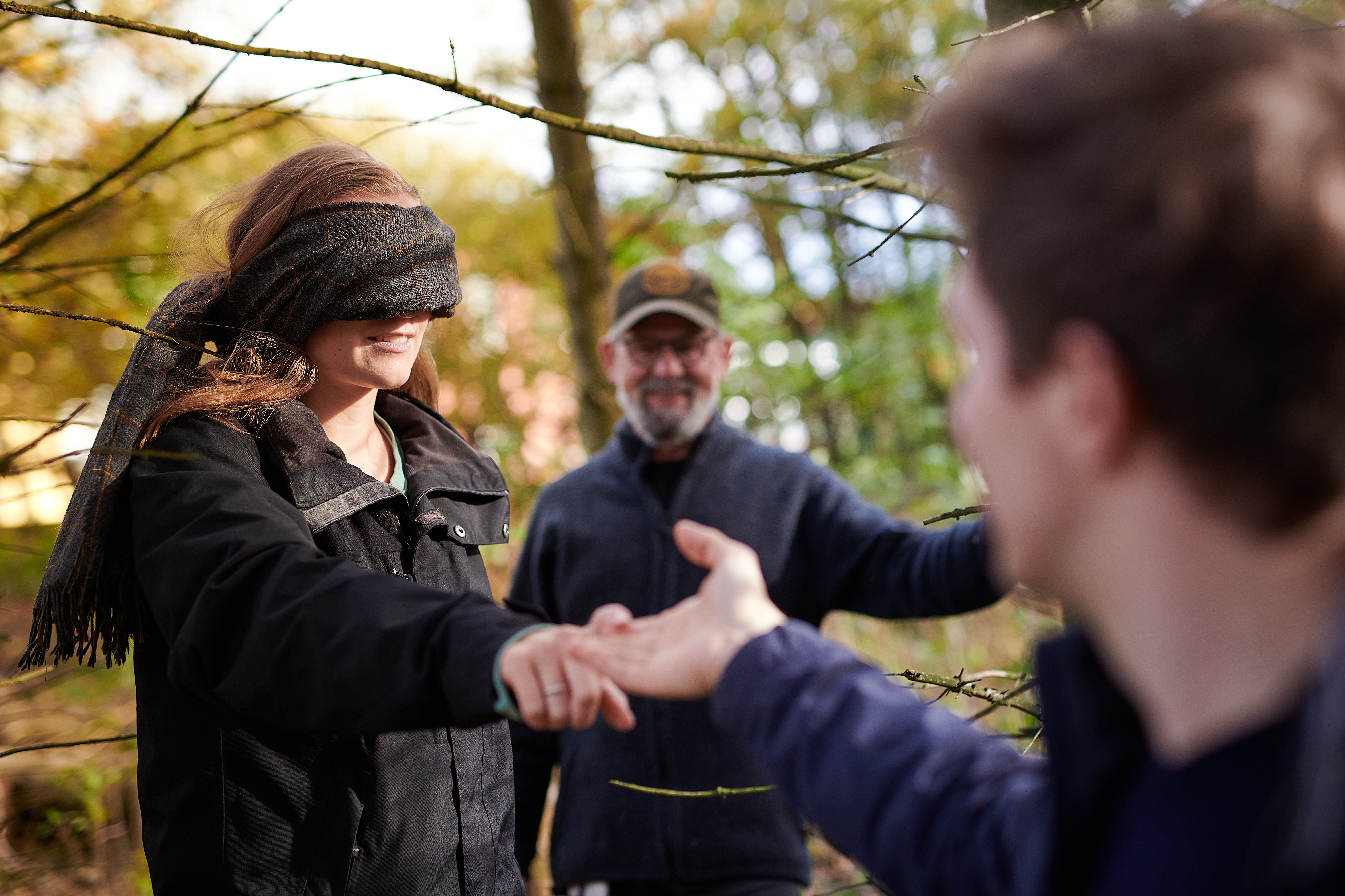 Ein junger Mann führt eine Frau an der Hand durch den Wald, im Hintergrund steht Waldtherapeut Stefan Alberts