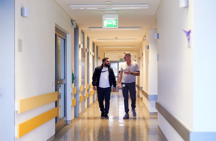 Zwei Männer gehen einen Klinikgang entlang.