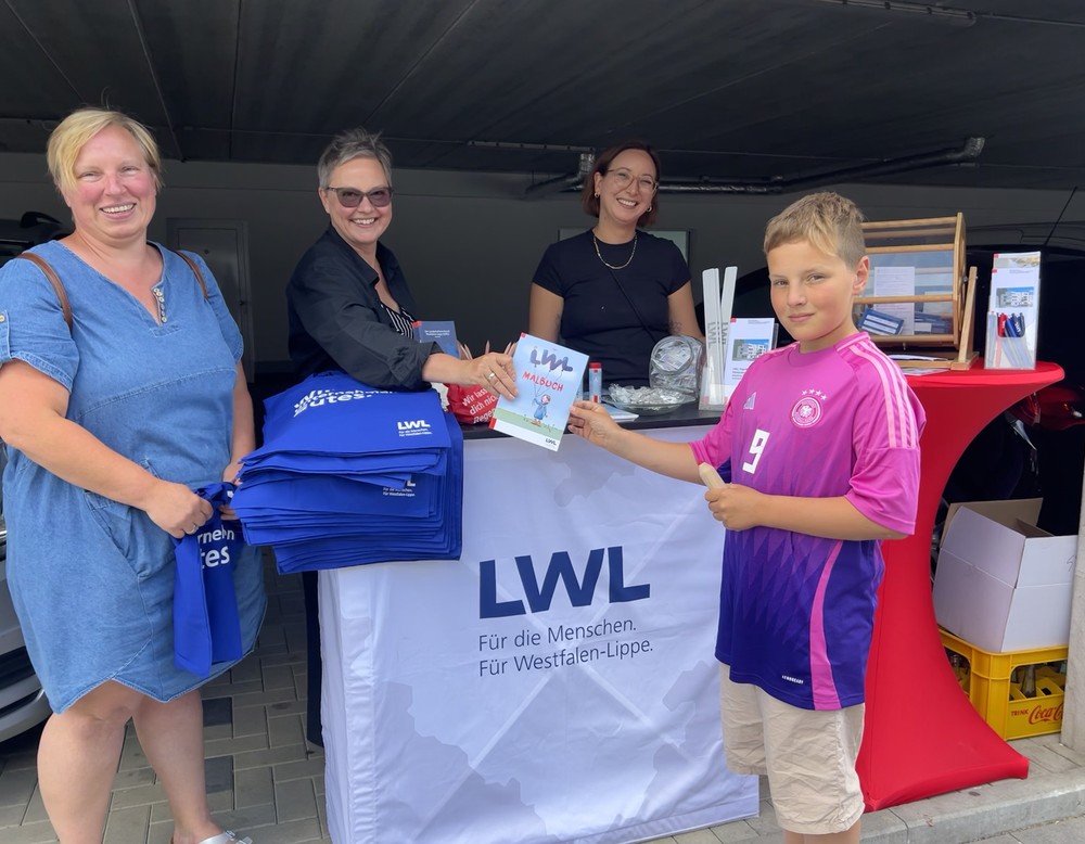 Kollegen vom LWL-Mobil vergeben kleine Geschenke an eine Besucherfamilie